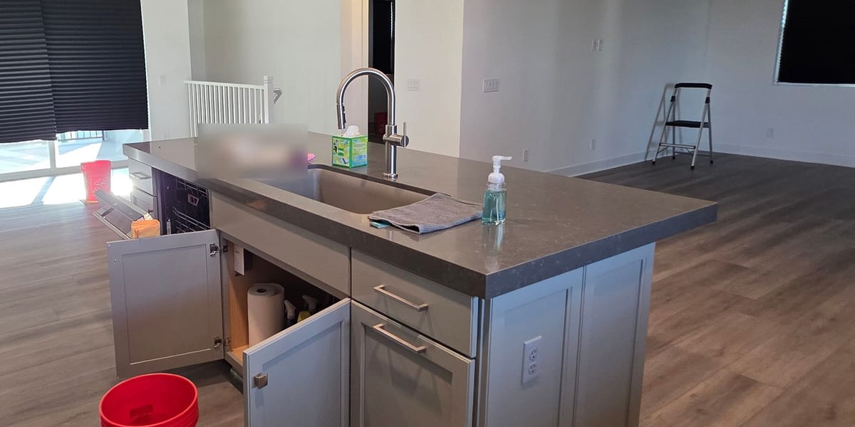 Open plan kitchen island with the sink cabinet doors open, a paper towel roll inside and a red bucket on the floor