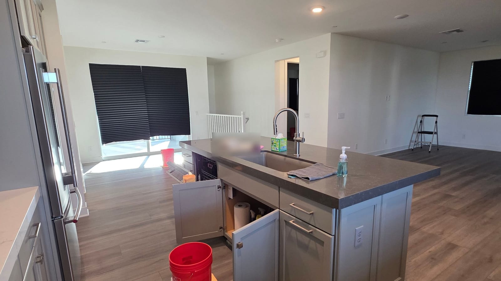 Bright open plan kitchen and living area in a newer home, with the island sink cabinet open and a bucket set out on the floor