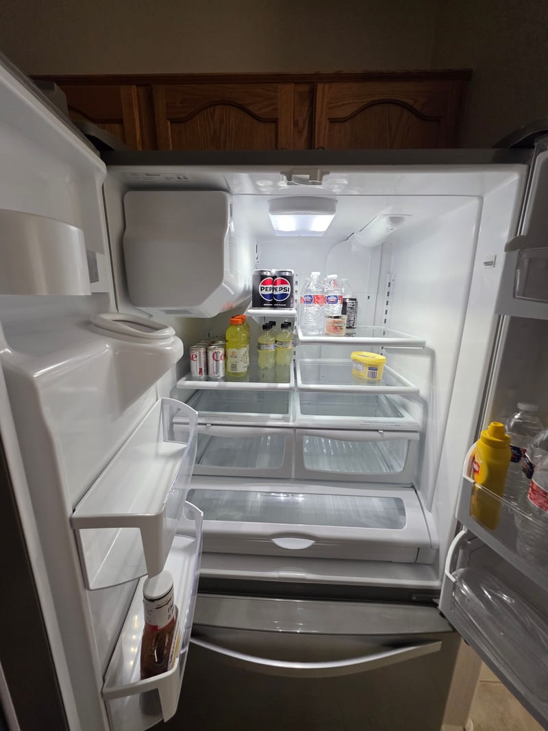 Open French door refrigerator with a lit interior holding bottled drinks, cans and a few condiments